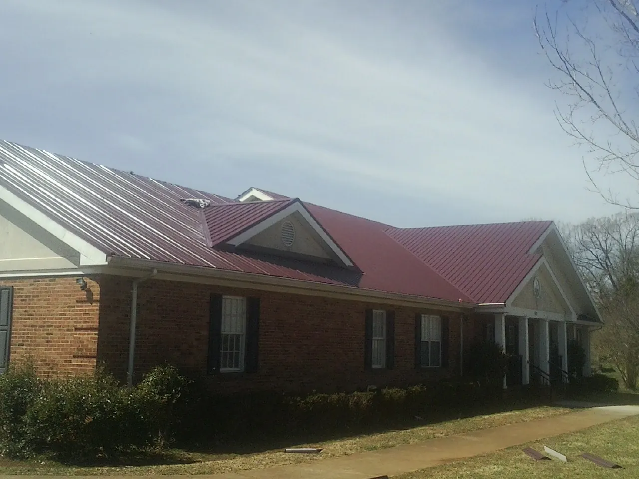 Red metal roof with gabled entries on a long brick building, from a Hail Damage Roof Repair job in Bristow
