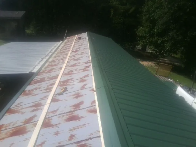 Old rusted panels beside newly installed green metal roofing — Wind Damage Roof Repair by Roofing Brothers in Bristow