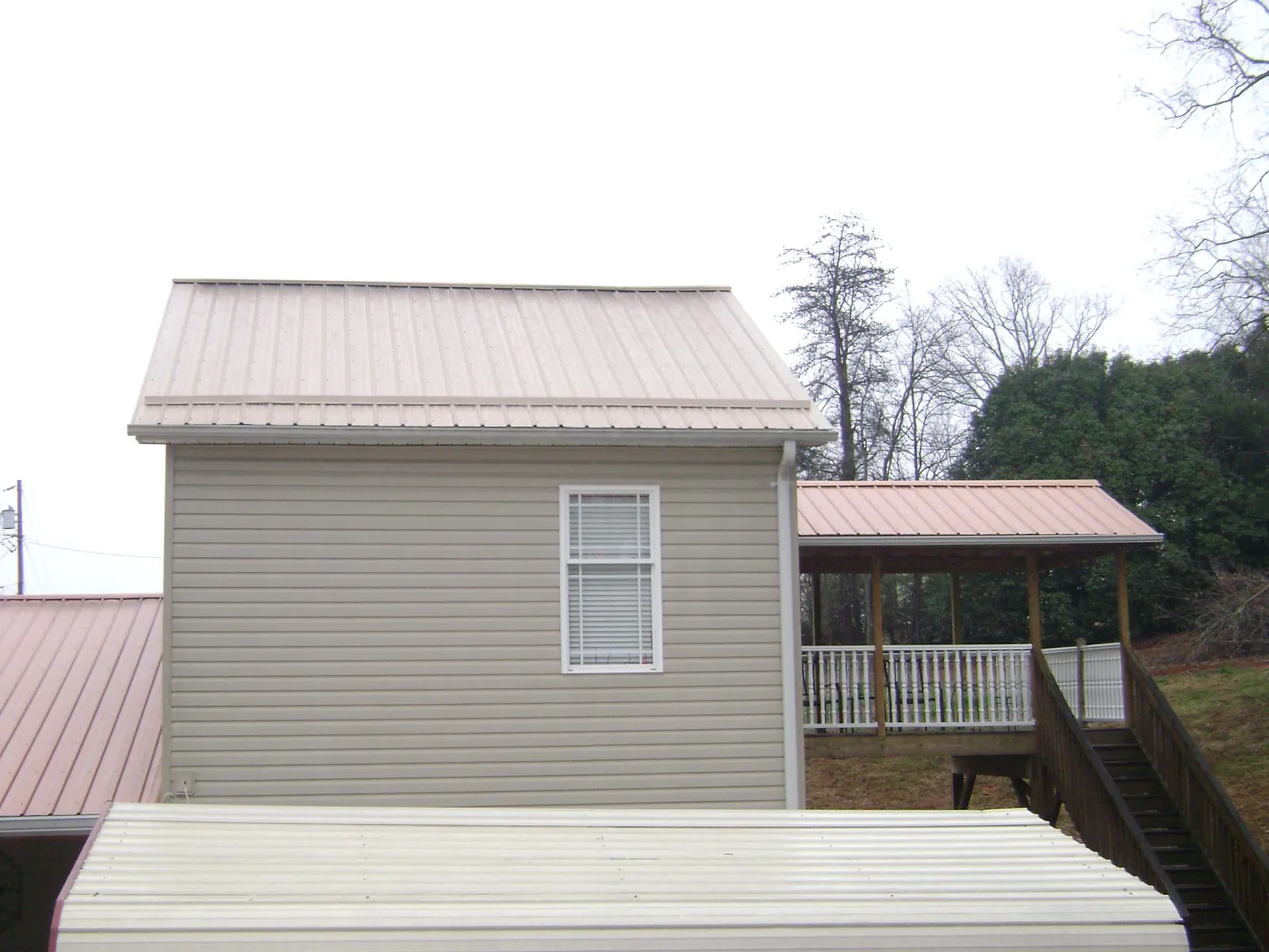 Tan metal roofs on a two story addition and attached porch, from a Roof Replacement job in Bristow